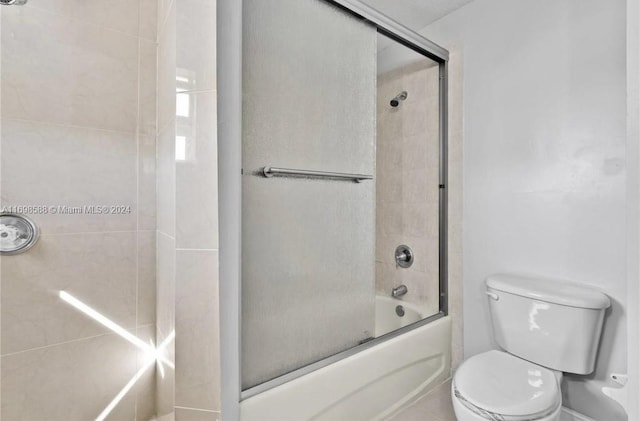 bathroom with toilet and bath / shower combo with glass door