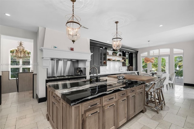 kitchen with french doors, an inviting chandelier, decorative backsplash, an island with sink, and decorative light fixtures