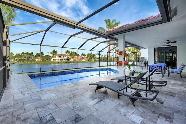 view of swimming pool with glass enclosure, ceiling fan, a patio area, and a water view