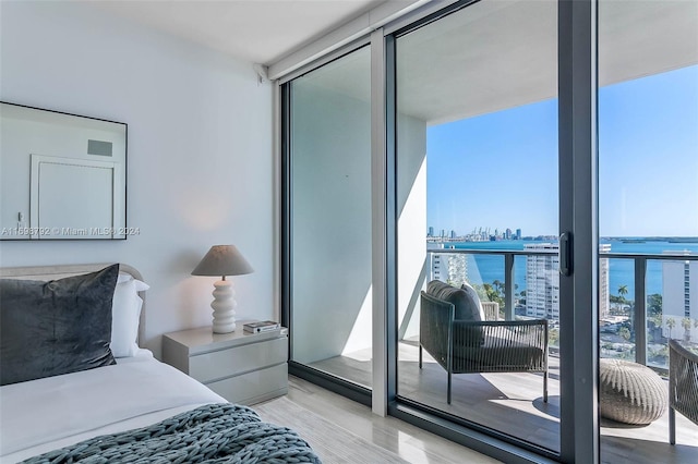 bedroom with floor to ceiling windows, a water view, and light wood-type flooring