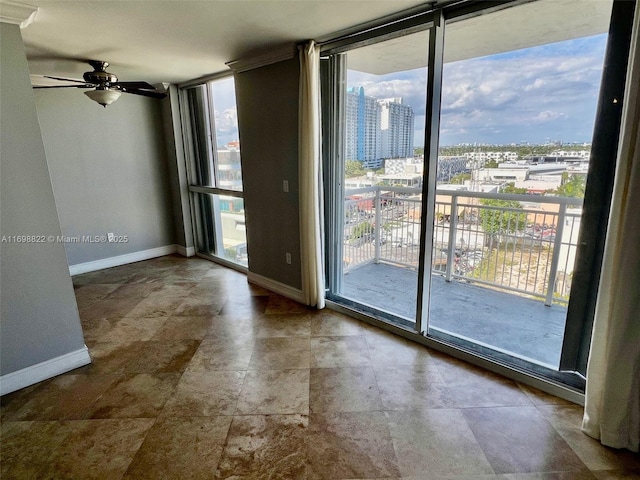 spare room with a ceiling fan, expansive windows, baseboards, and a view of city