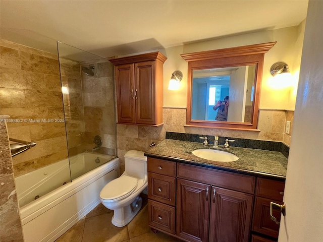 bathroom with toilet, tile patterned floors,  shower combination, vanity, and tile walls