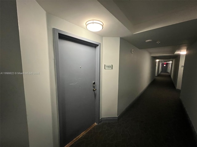 corridor with baseboards and dark carpet