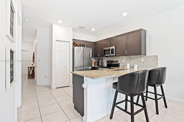 kitchen with stainless steel appliances, tasteful backsplash, kitchen peninsula, a kitchen bar, and dark brown cabinets