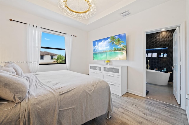 bedroom with a chandelier, light wood-type flooring, and a raised ceiling