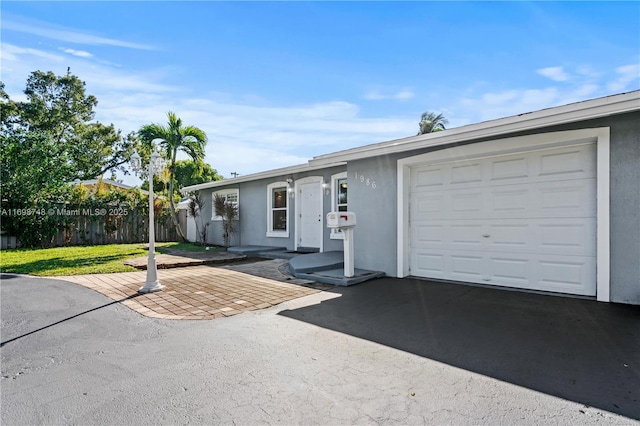 ranch-style house with aphalt driveway, a front yard, fence, and stucco siding