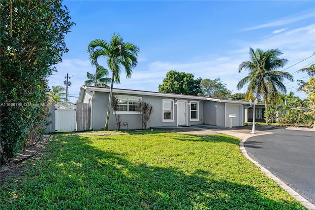 view of front of property featuring driveway, an attached garage, fence, a front lawn, and stucco siding