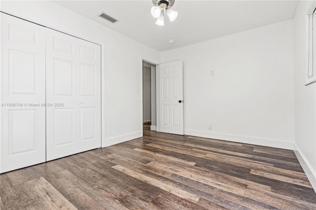 unfurnished bedroom featuring baseboards, a closet, visible vents, and wood finished floors