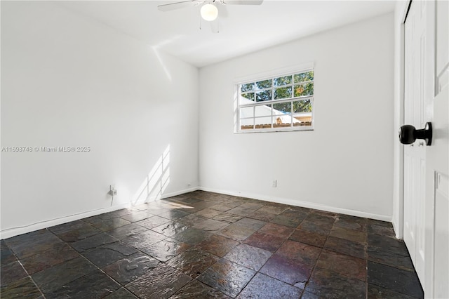 spare room featuring stone tile floors, baseboards, and ceiling fan