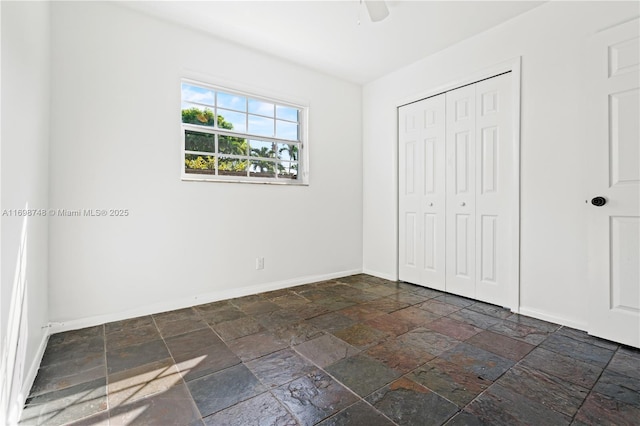 unfurnished bedroom with a closet, stone tile flooring, and baseboards