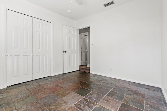 unfurnished bedroom with ceiling fan, stone tile floors, visible vents, baseboards, and a closet