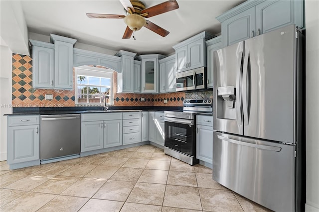 kitchen featuring stainless steel appliances, tasteful backsplash, dark countertops, and glass insert cabinets