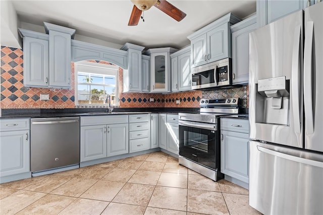 kitchen with ceiling fan, stainless steel appliances, a sink, tasteful backsplash, and dark countertops