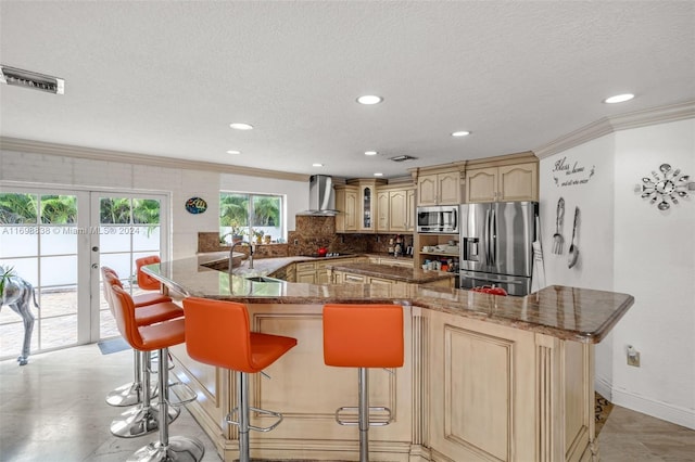 kitchen featuring wall chimney exhaust hood, crown molding, a textured ceiling, a kitchen bar, and appliances with stainless steel finishes