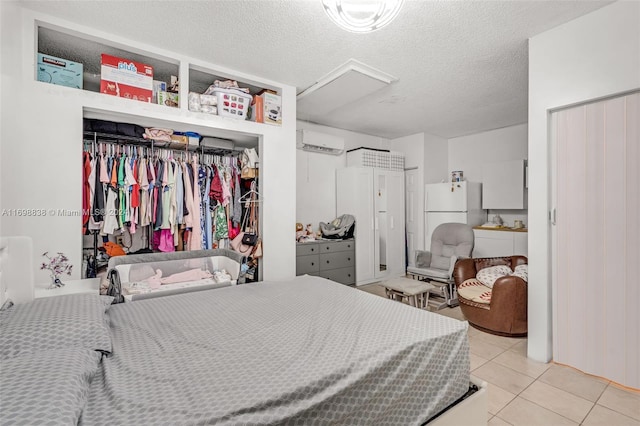 tiled bedroom featuring a wall mounted AC, white fridge, and a textured ceiling