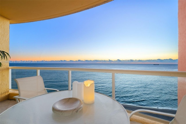 balcony at dusk featuring a water view