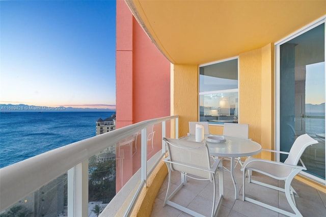 balcony at dusk featuring a water view