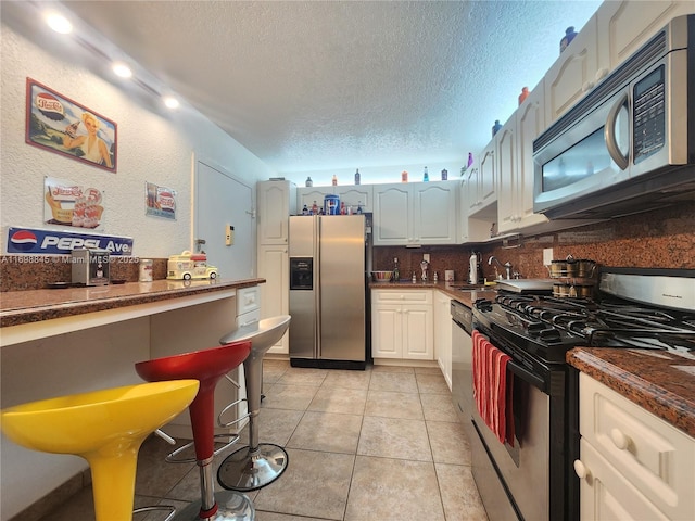 kitchen featuring a textured ceiling, white cabinets, appliances with stainless steel finishes, sink, and light tile patterned floors