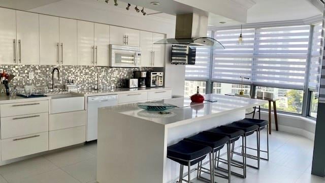 kitchen with decorative backsplash, white appliances, wall chimney range hood, sink, and white cabinets