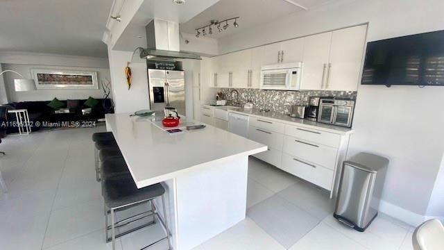 kitchen with decorative backsplash, white appliances, white cabinetry, and a breakfast bar area