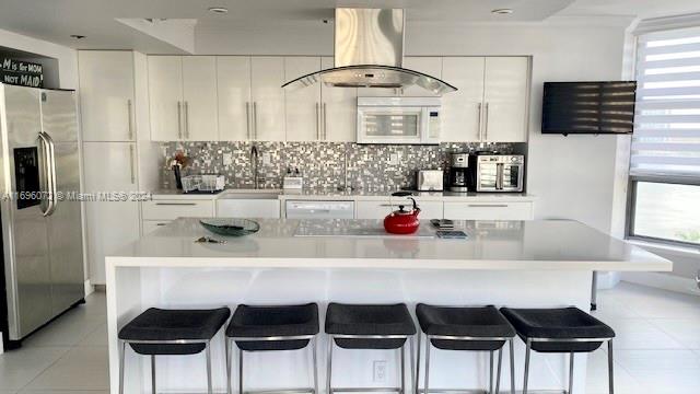 kitchen featuring tasteful backsplash, island exhaust hood, a kitchen bar, white cabinets, and appliances with stainless steel finishes