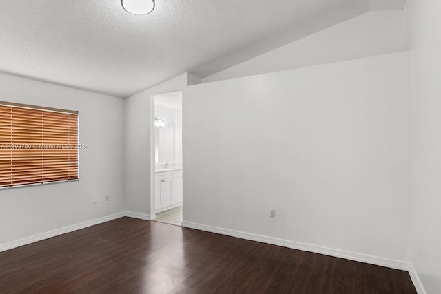 empty room with a textured ceiling, dark hardwood / wood-style flooring, and lofted ceiling