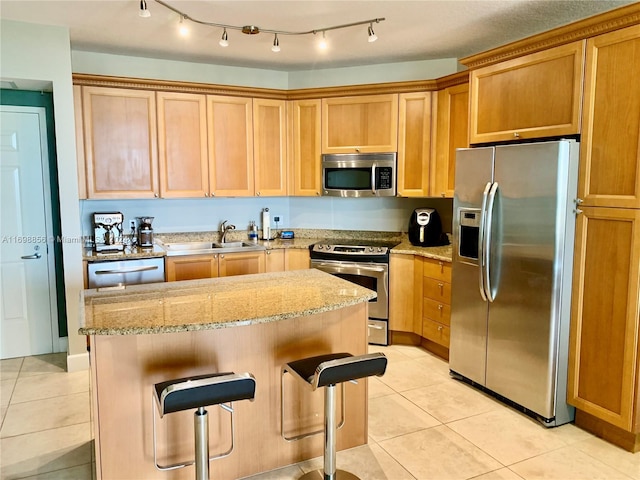 kitchen with sink, light tile patterned floors, appliances with stainless steel finishes, light stone counters, and a breakfast bar area