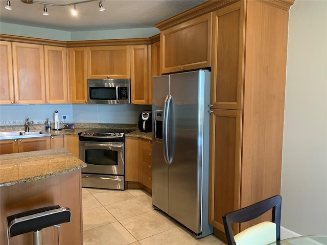 kitchen with sink, stainless steel appliances, light stone counters, a textured ceiling, and light tile patterned floors