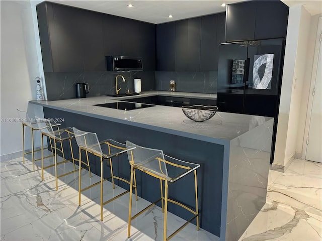 kitchen featuring black electric stovetop, sink, tasteful backsplash, a kitchen bar, and kitchen peninsula