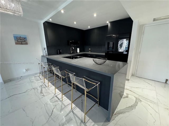 kitchen with kitchen peninsula, a kitchen bar, light stone countertops, black appliances, and a notable chandelier