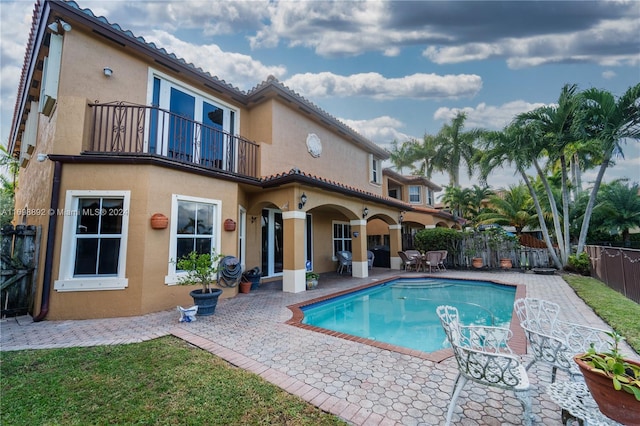 rear view of house with a fenced in pool, a patio area, and a balcony