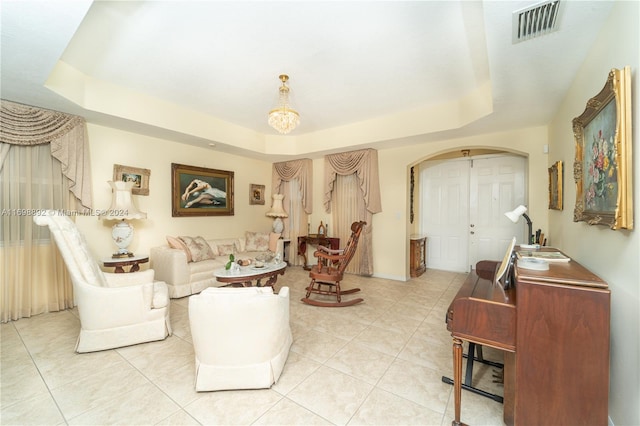 living room with a notable chandelier, light tile patterned floors, and a tray ceiling