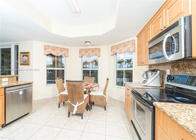 kitchen featuring light stone countertops, stainless steel appliances, a tray ceiling, light brown cabinetry, and light tile patterned floors