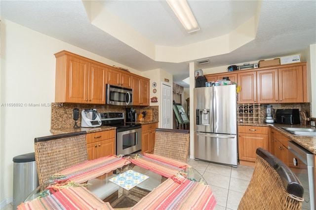 kitchen featuring sink, stainless steel appliances, a raised ceiling, dark stone counters, and light tile patterned floors