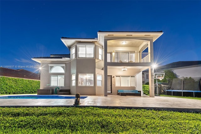 back house at twilight with a patio area, a balcony, an outdoor hangout area, and a trampoline