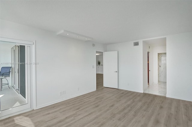 spare room with a textured ceiling and light hardwood / wood-style flooring