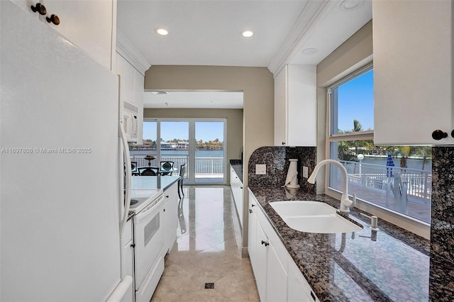 kitchen featuring sink, white appliances, a water view, white cabinets, and dark stone counters