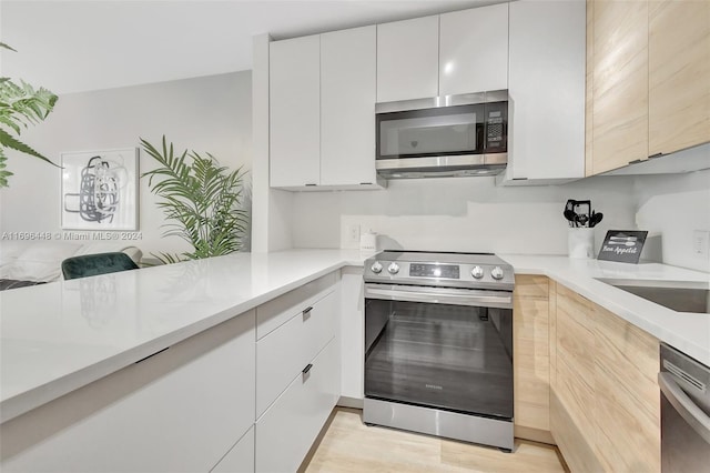 kitchen featuring white cabinets, light hardwood / wood-style floors, kitchen peninsula, and appliances with stainless steel finishes