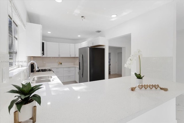 kitchen featuring kitchen peninsula, stainless steel fridge, sink, and white cabinets