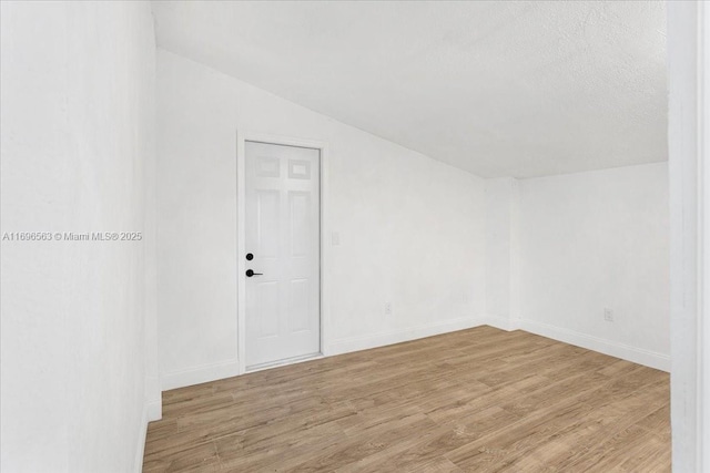 spare room featuring a textured ceiling, light hardwood / wood-style floors, and lofted ceiling