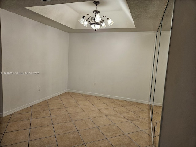 spare room with a notable chandelier, a raised ceiling, a textured ceiling, and light tile patterned floors