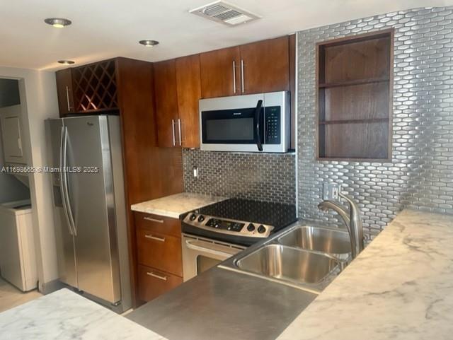 kitchen featuring sink, decorative backsplash, washer / dryer, and appliances with stainless steel finishes