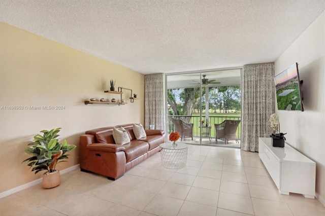 living room with light tile patterned flooring, a wall of windows, ceiling fan, and a textured ceiling