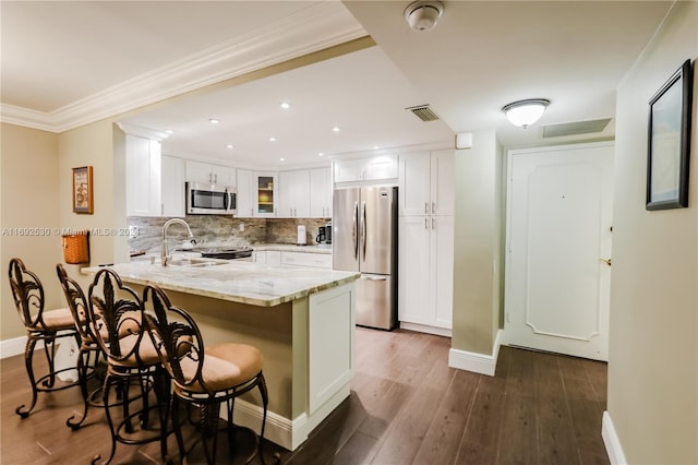 kitchen with white cabinetry, stainless steel appliances, a kitchen breakfast bar, dark hardwood / wood-style floors, and kitchen peninsula