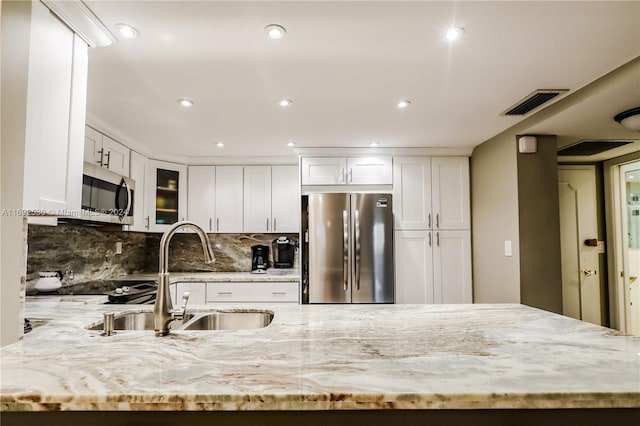 kitchen with white cabinets, sink, decorative backsplash, light stone countertops, and appliances with stainless steel finishes