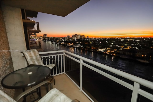 balcony at dusk featuring a water view