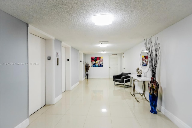 hall with light tile patterned floors, a textured ceiling, and elevator