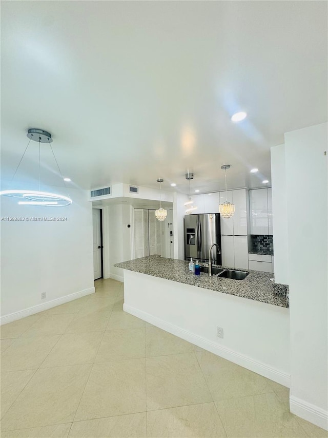 kitchen with white cabinets, sink, stainless steel fridge, light stone countertops, and kitchen peninsula