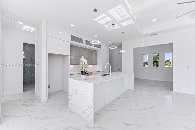 kitchen featuring light stone counters, sink, pendant lighting, white cabinets, and an island with sink