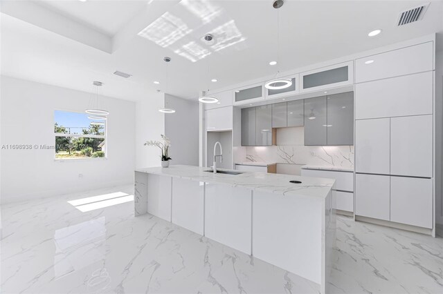 kitchen with light stone countertops, tasteful backsplash, gray cabinetry, sink, and pendant lighting